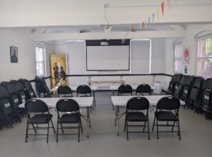 A picture of the library annex, which includes tables, chairs and the library's projector and screen can be seen in the background. 