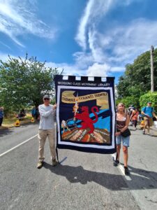 A man and a women stand holding a banner representing the WCML against a sunny sky.